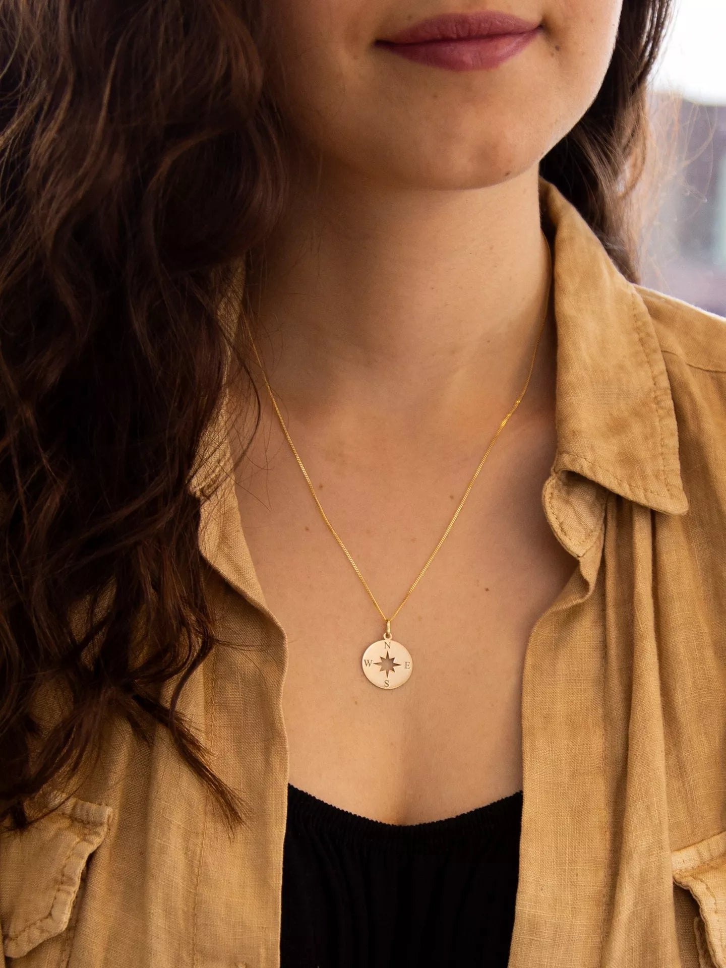9ct Yellow Gold Compass Pendant from Harrogate Jewellers, a bespoke piece perfect for gifting, featured on a blurred urban background.