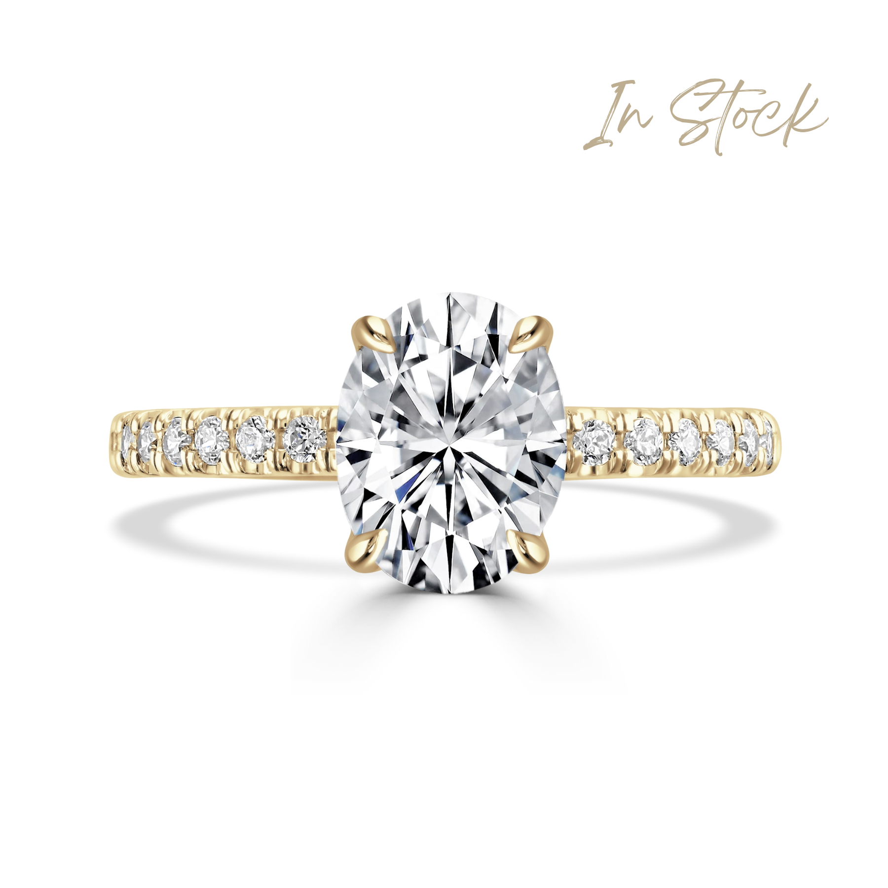 A yellow gold oval solitaire engagement ring featuring a large oval-cut center diamond and a pavé-set diamond band, shown on a clean white background with an 'In Stock' text overlay in the top right.